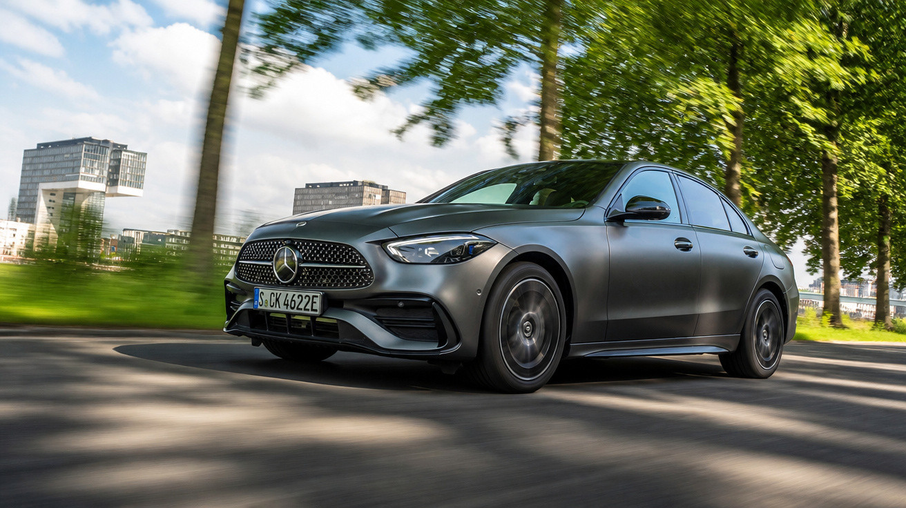 Carro preto Mercedes-Benz a circular numa estrada urbana com árvores e edifícios ao fundo.