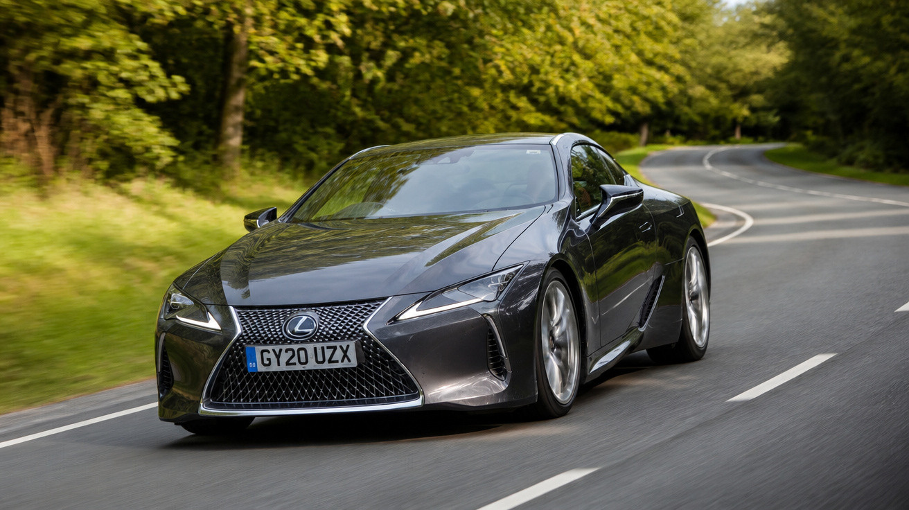 Carro desportivo cinzento Lexus a circular numa estrada rodeada de árvores verdes.
