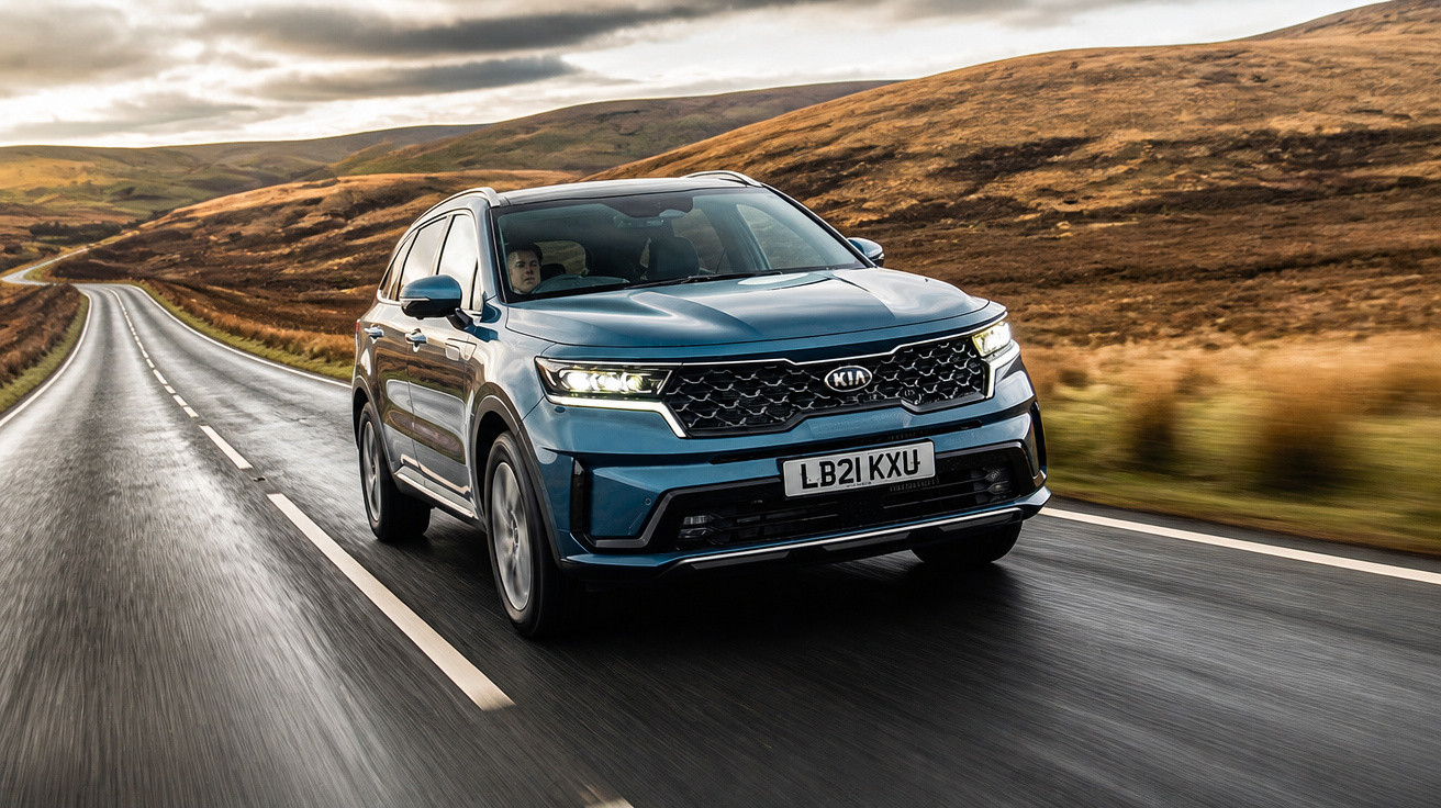 Carro Kia SUV azul a circular numa estrada molhada entre colinas e céu nublado ao entardecer.