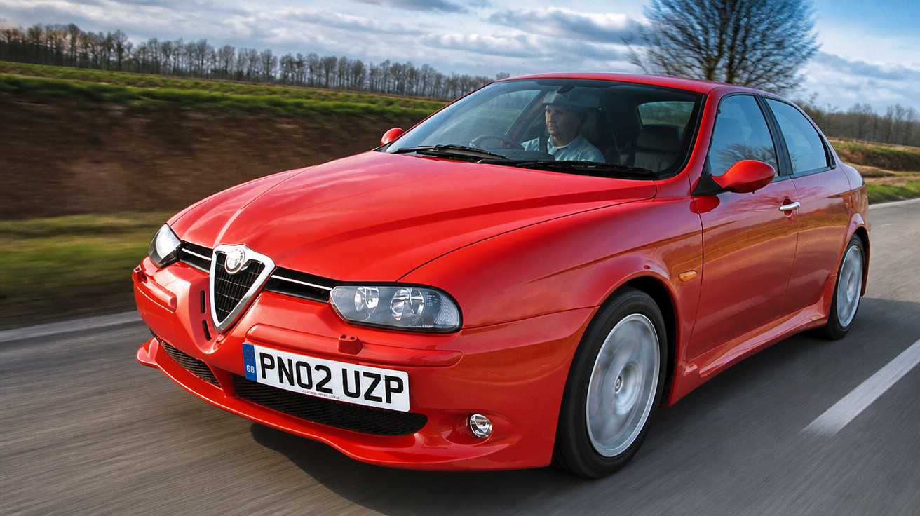 Carro desportivo vermelho Alfa Romeo a circular numa estrada com céu nublado e árvores ao fundo.