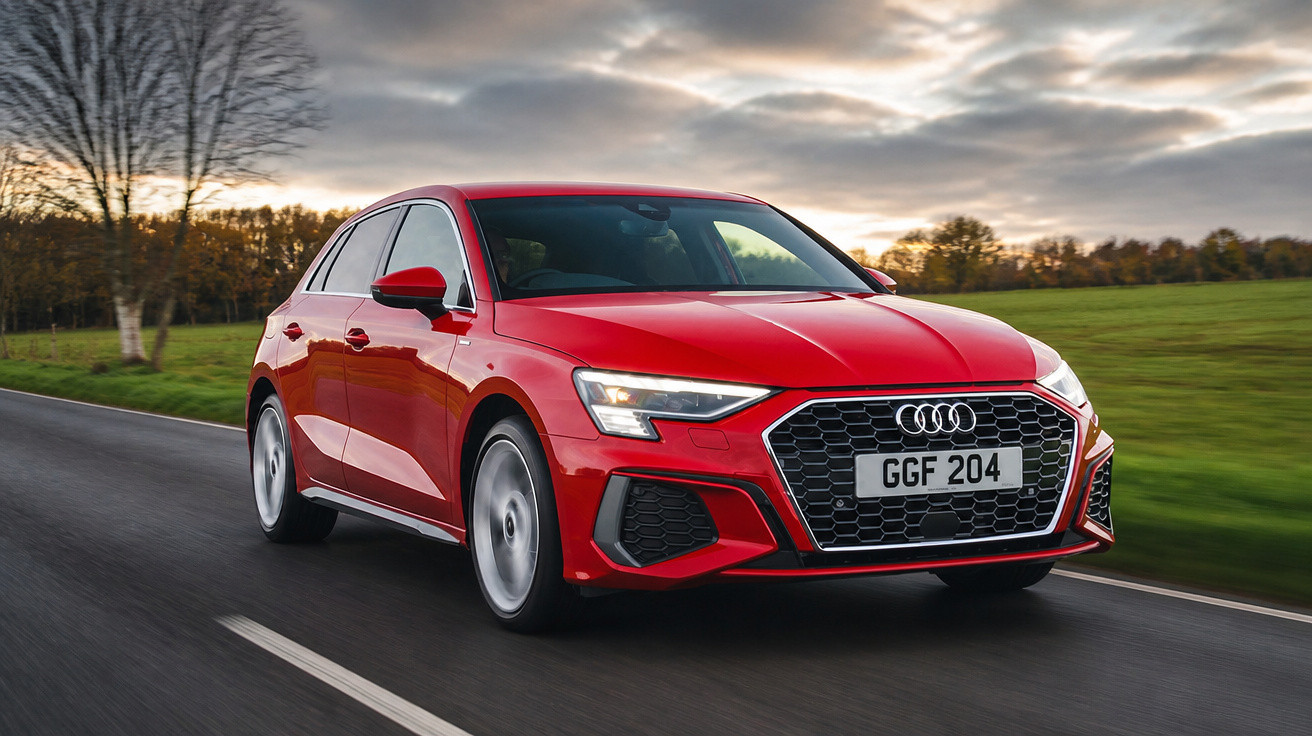 Carro Audi vermelho em estrada asfaltada, com céu nublado e campo verde ao fundo.