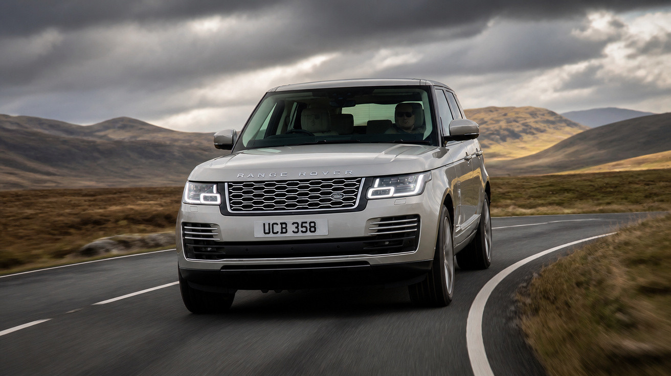 Carro Range Rover cinzento conduzido numa estrada sinuosa em zona montanhosa sob céu nublado.