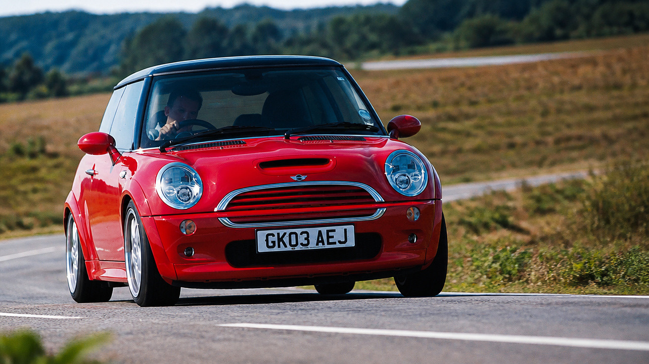 Carro Mini Cooper vermelho a circular numa estrada sinuosa com paisagem rural ao fundo.