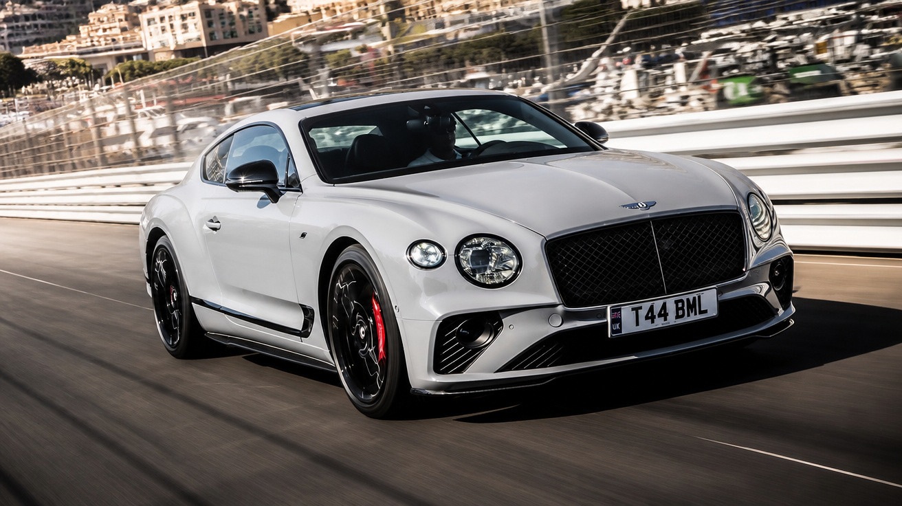 Carro desportivo Bentley branco em alta velocidade numa pista de corrida urbana.