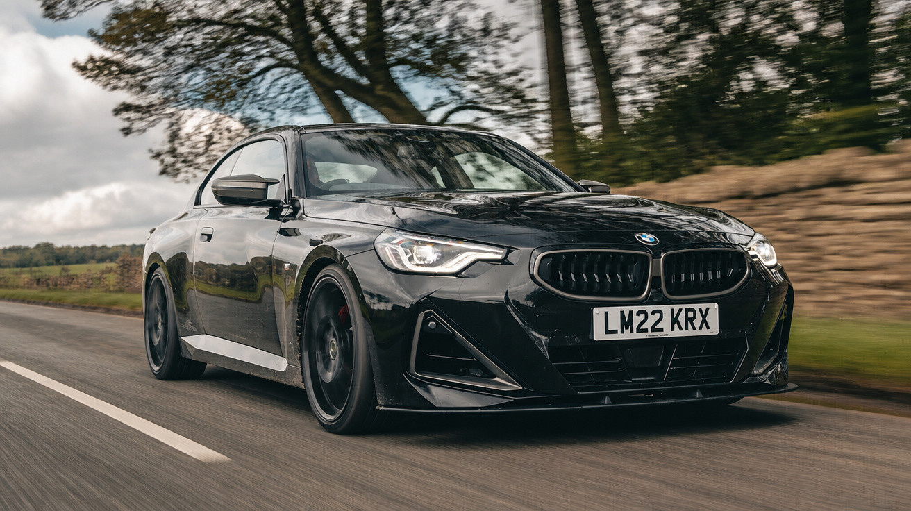 Carro desportivo preto BMW em movimento numa estrada rural com árvores e céu nublado.