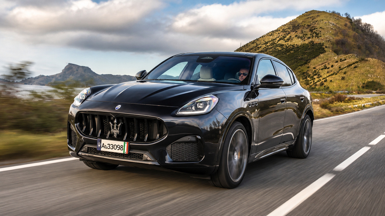 Carro preto Maserati em movimento numa estrada com montanhas ao fundo e céu nublado.