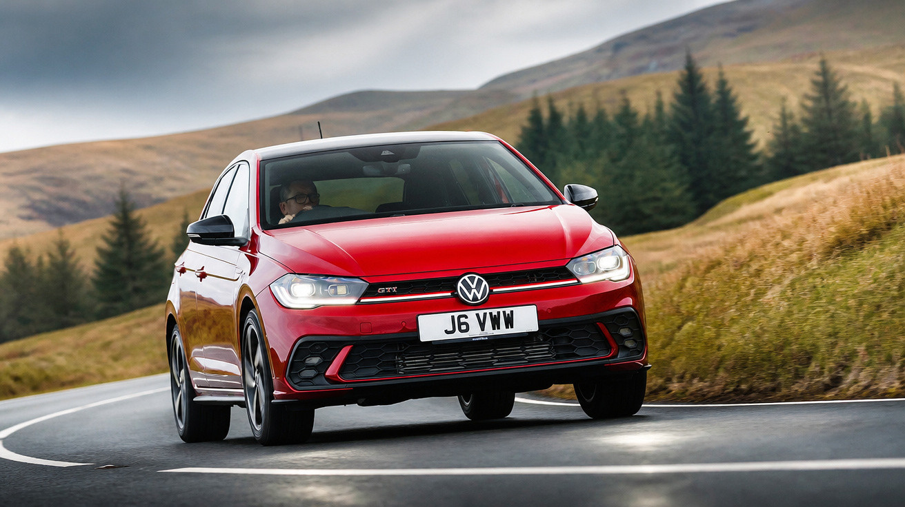 Carro vermelho Volkswagen GTI a curvar numa estrada rodeada de relva e árvores em dia nublado.