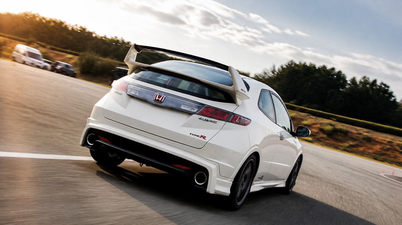 Carro Honda Civic Type R branco em movimento numa estrada sinuosa ao ar livre ao entardecer.