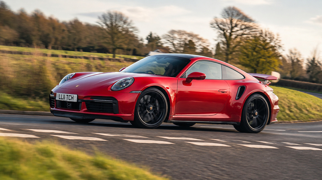 Carro desportivo vermelho Porsche a circular numa estrada em curva com paisagem de árvores ao fundo.