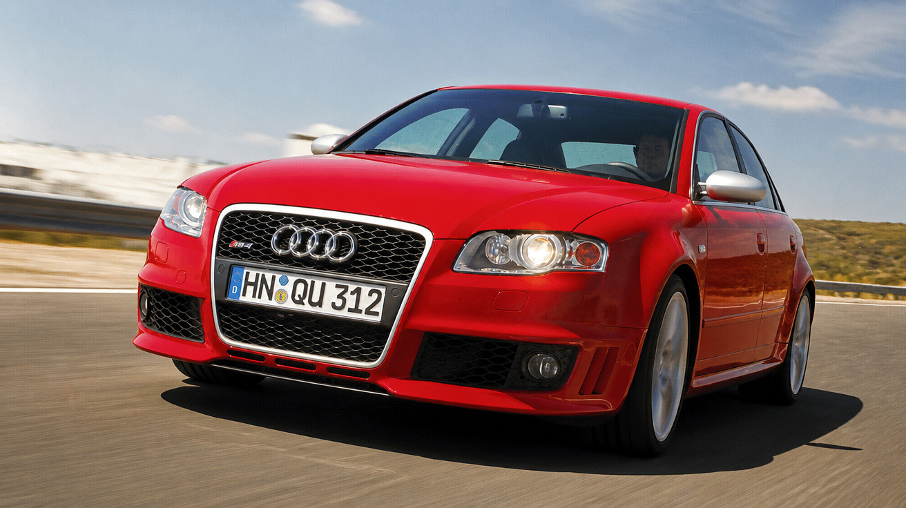 Carro Audi RS4 vermelho em movimento numa estrada sob céu nublado.