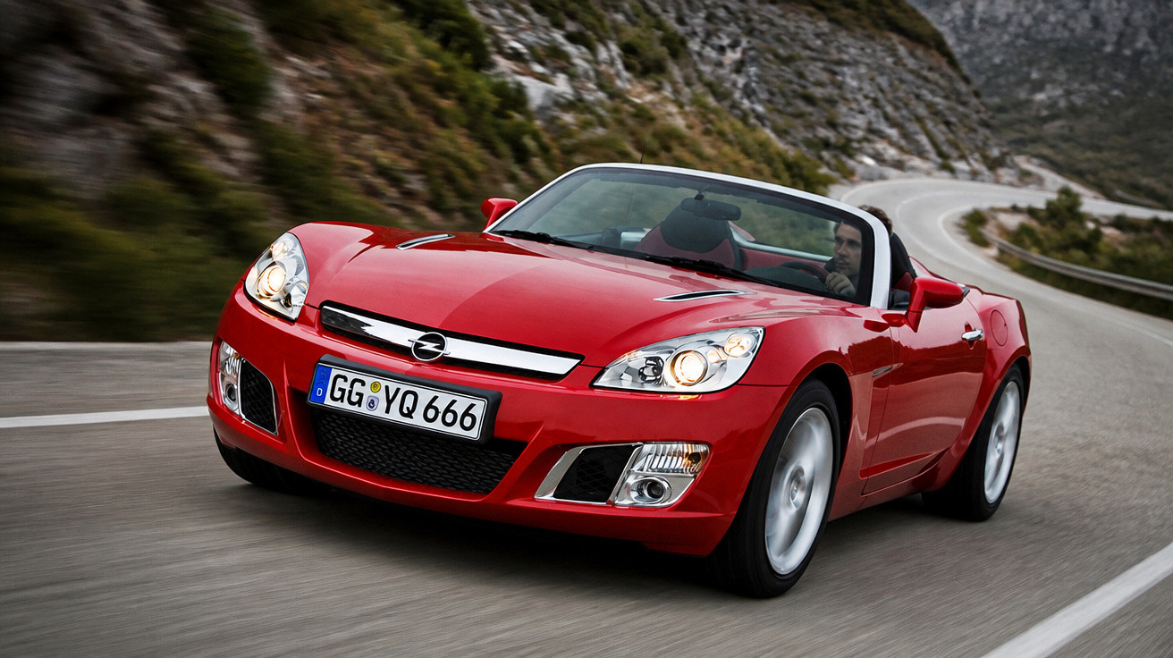 Carro desportivo conversível vermelho a circular numa estrada de montanha com curvas.