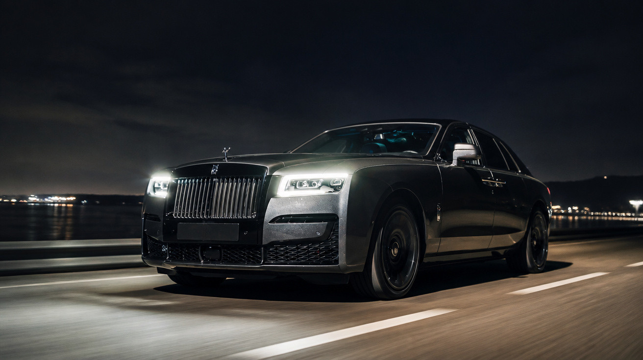 Carro de luxo preto a conduzir de noite numa estrada com luzes urbanas ao fundo.